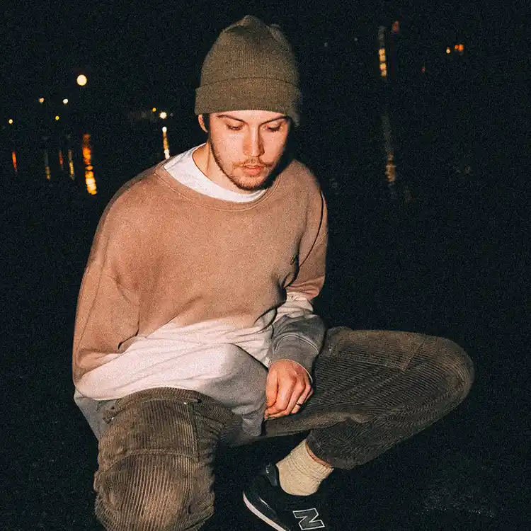 Image of the artist at night time against a long grass backdrop.